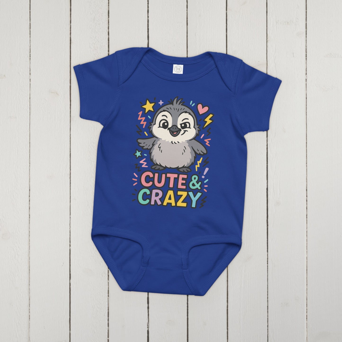 Blue baby onesie with a penguin graphic and 'Cute & Crazy' text on a wooden surface