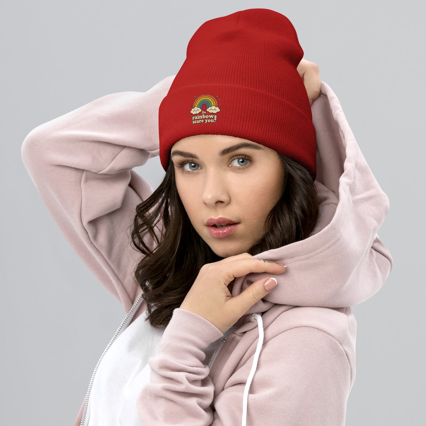 Woman wearing a red beanie with text and a pink hoodie on a gray background