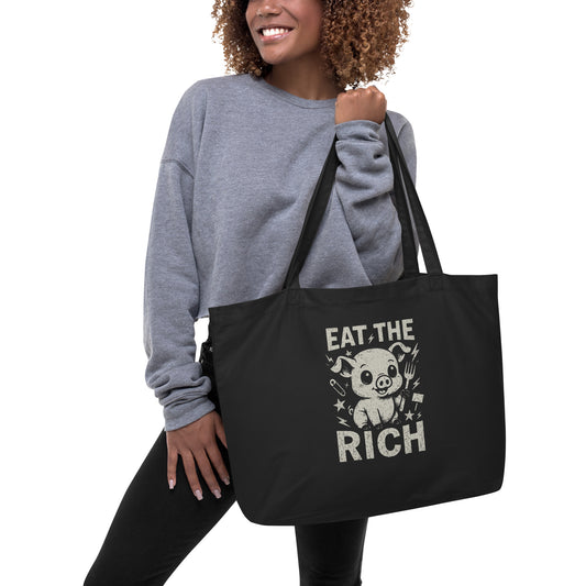 Person holding a black tote bag with 'Eat the Rich' graphic design.