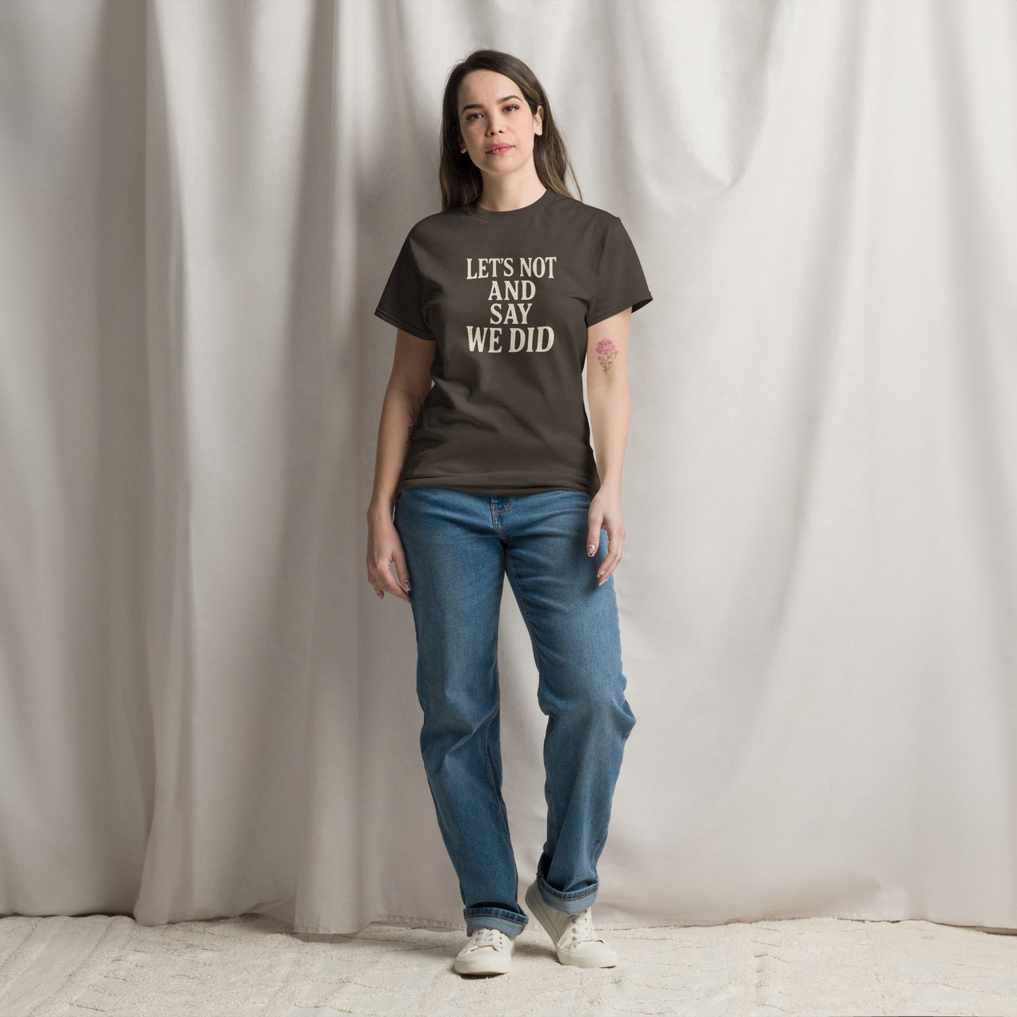 Person wearing a brown t-shirt with text and blue jeans standing against a plain background