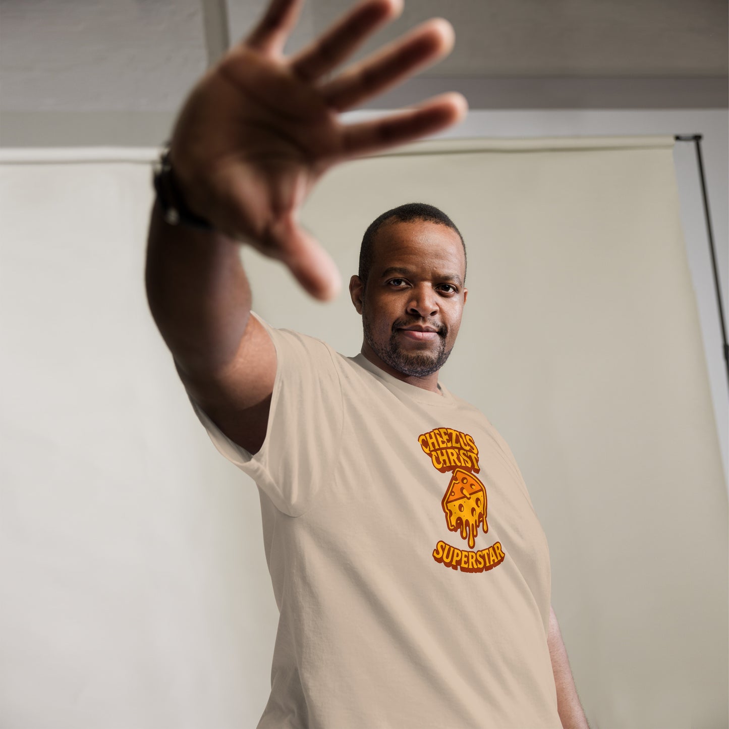 Man wearing a beige t-shirt with a logo and text, standing against a plain background
