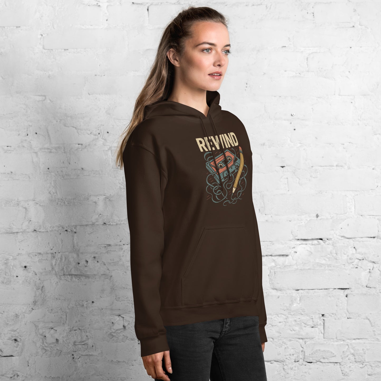 Woman wearing a brown hoodie with a graphic design against a white brick wall.
