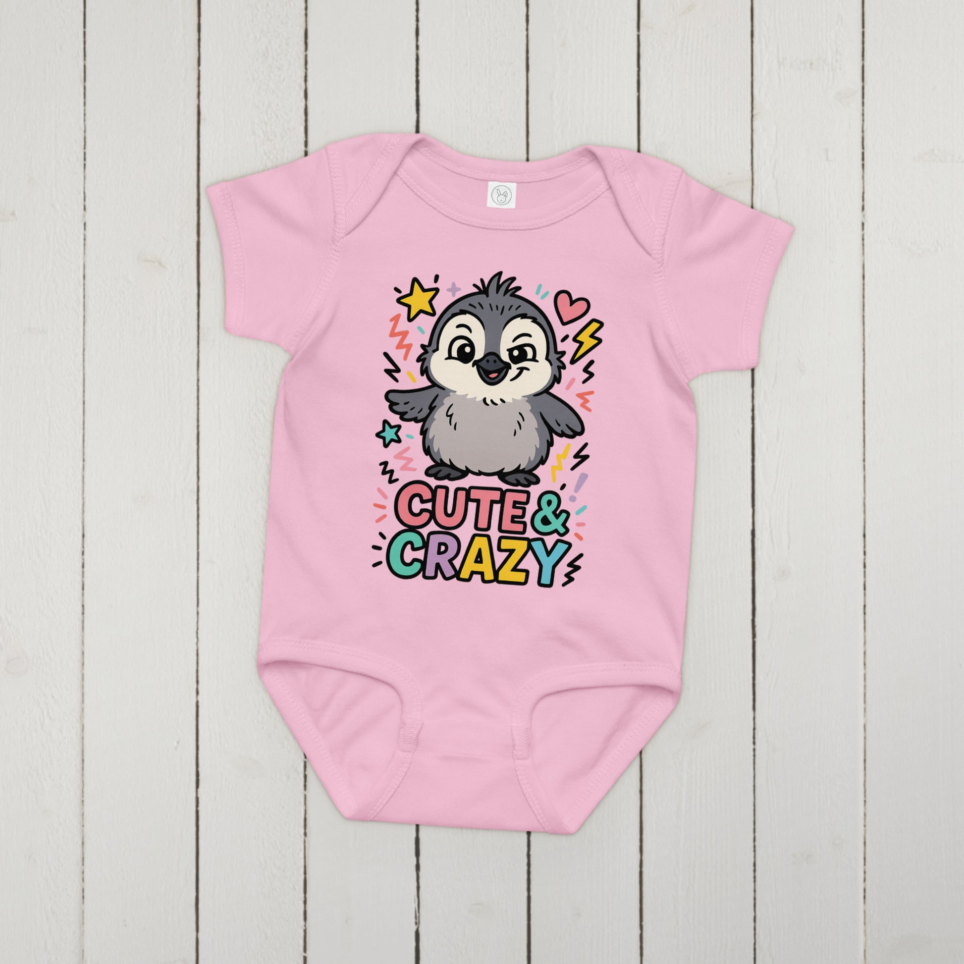 Pink baby onesie with a penguin graphic and 'Cute & Crazy' text on a wooden surface
