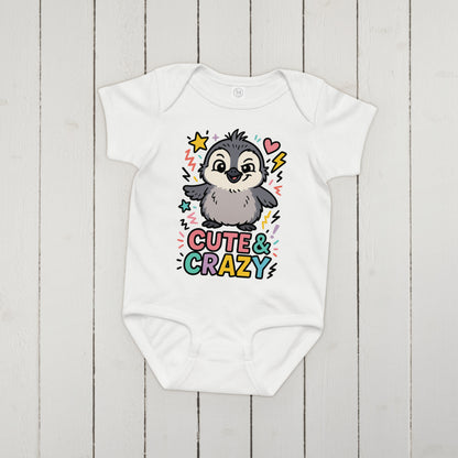 White baby onesie with a penguin design and 'Cute & Crazy' text on a wooden surface