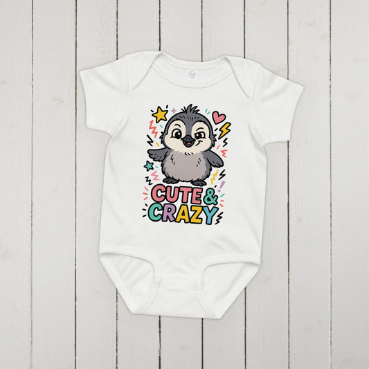 White baby onesie with a penguin design and 'Cute & Crazy' text on a wooden surface