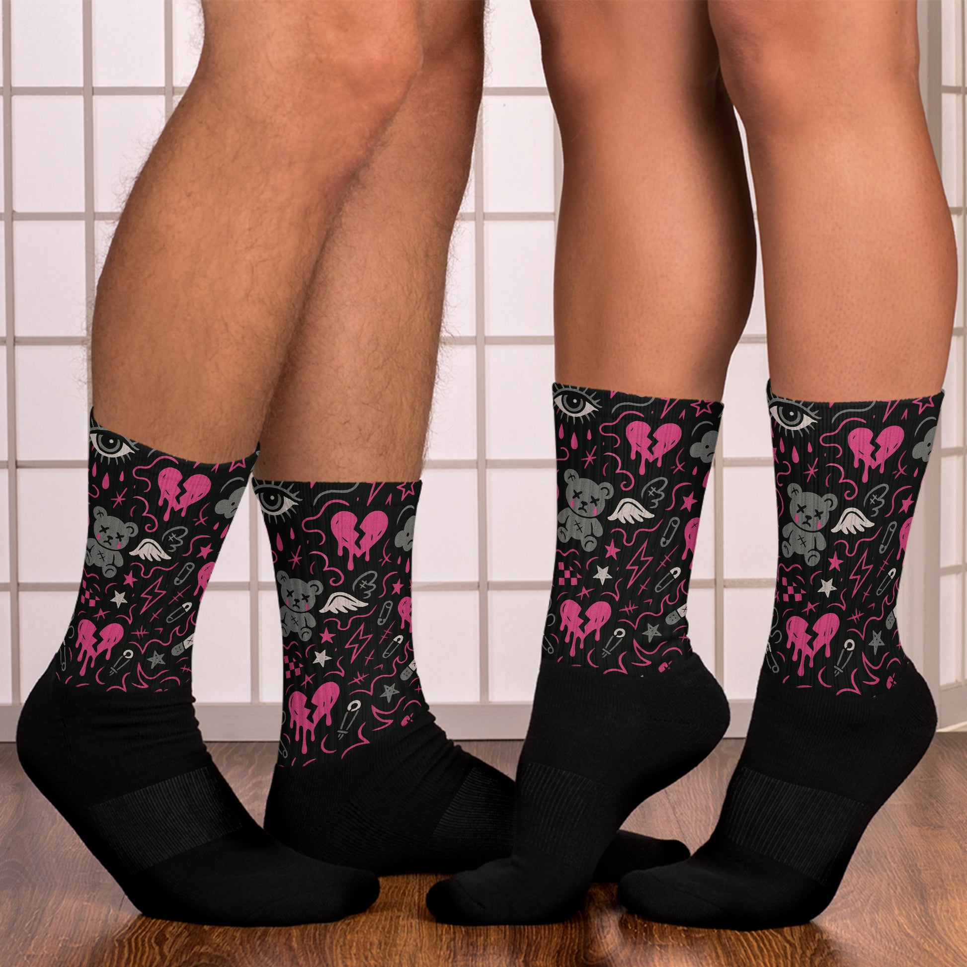 Black socks with pink and gray designs worn by two people on a tiled floor.