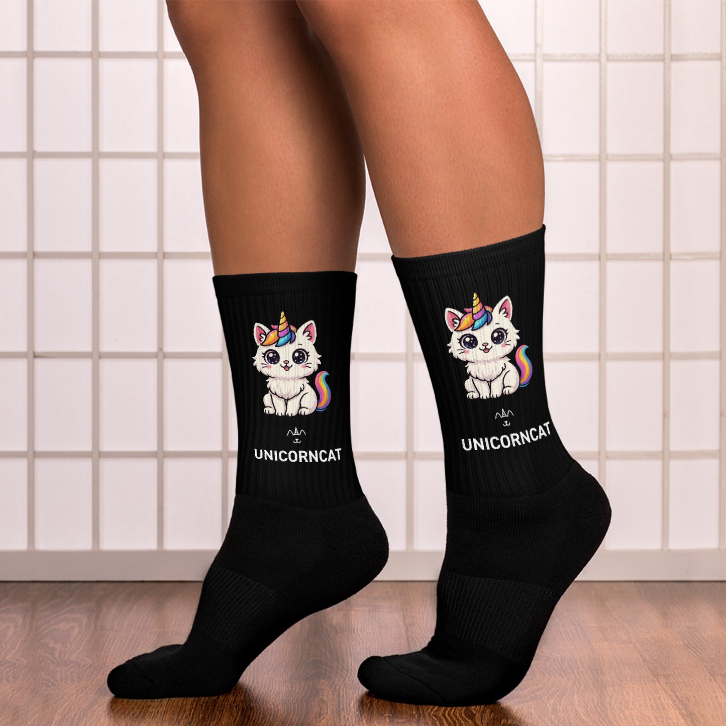 Black socks with unicorn and cat design worn by a person on a tiled floor.