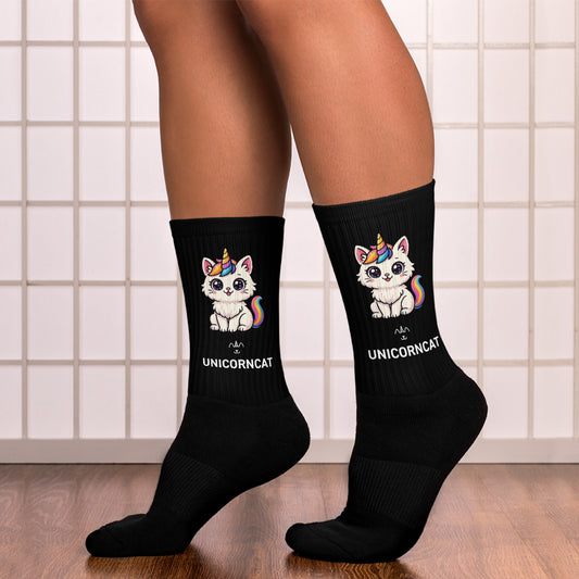 Black socks with unicorn and cat design worn by a person on a tiled floor.