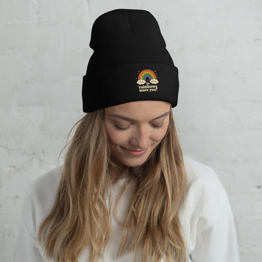 Person wearing a black beanie with a rainbow design and text against a light gray background