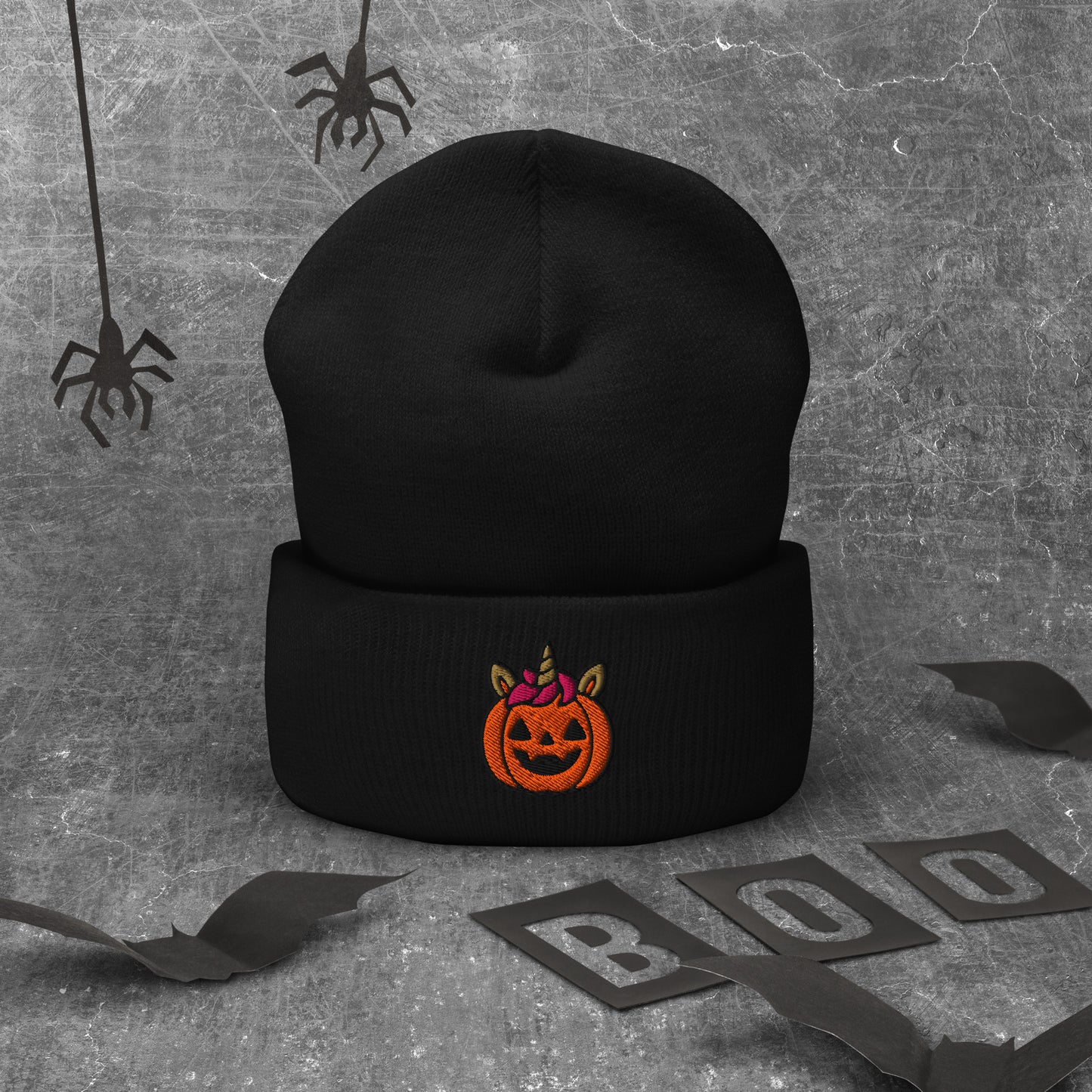 Black beanie with Halloween pumpkin design on a textured gray background with spider webs and 'BOO' letters.