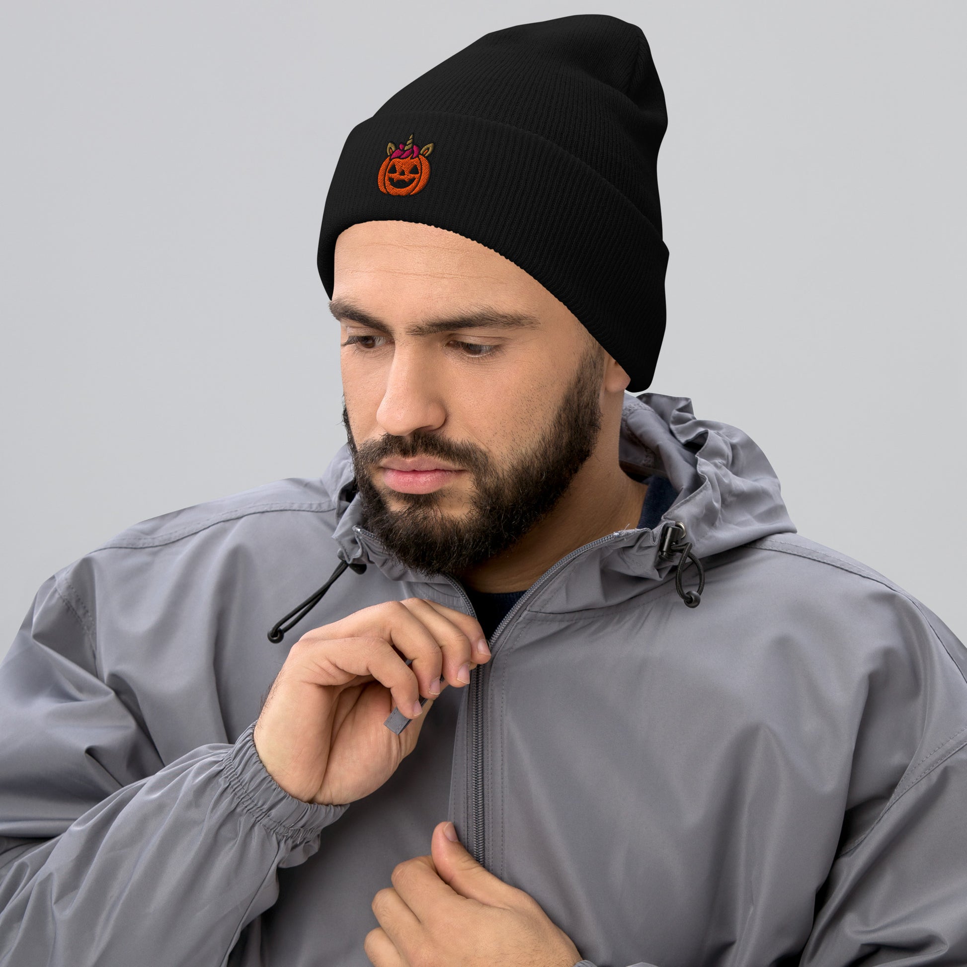 Man wearing a black beanie with a logo and a gray jacket on a light gray background