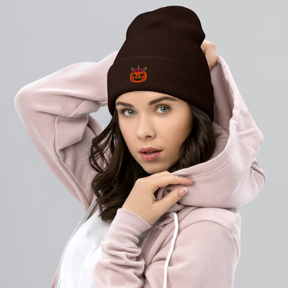 Woman wearing a pink hoodie and brown beanie with a pumpkin design on a gray background