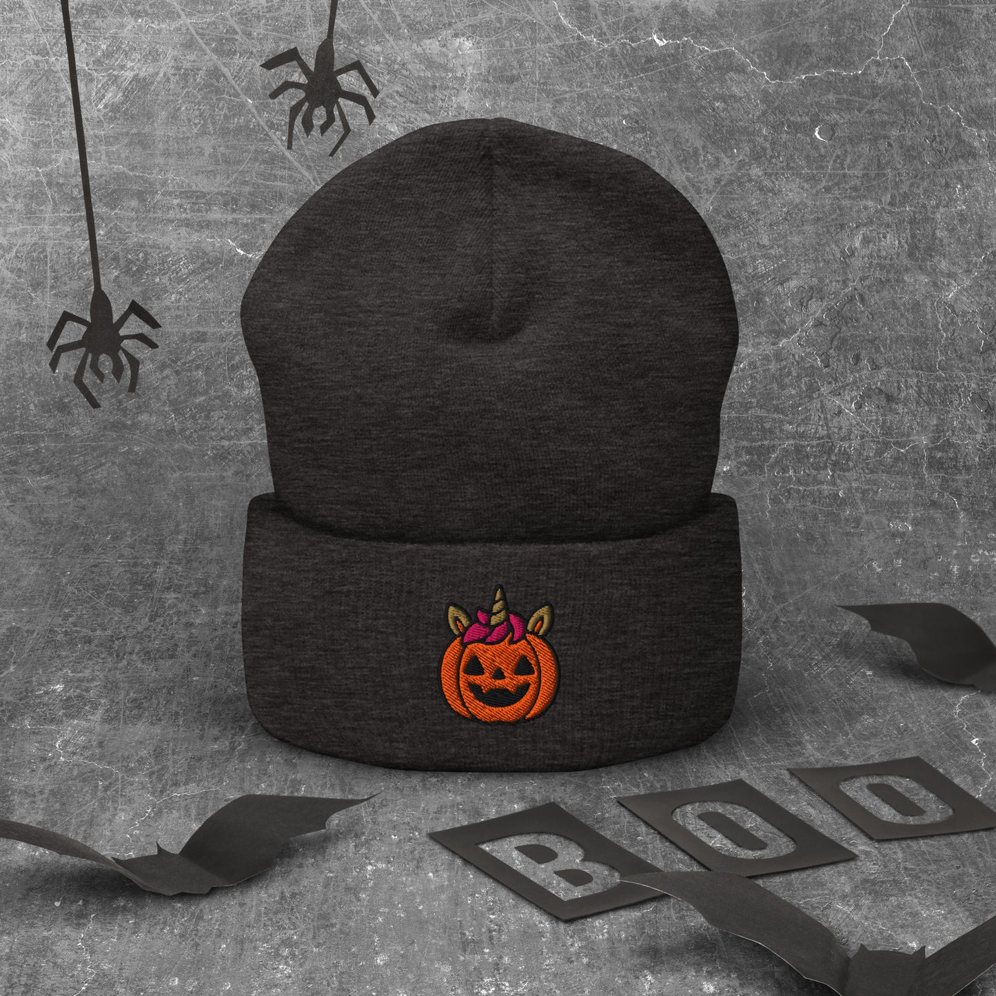 Black beanie with Halloween pumpkin design on a textured gray background with spider webs and 'BOO' letters.