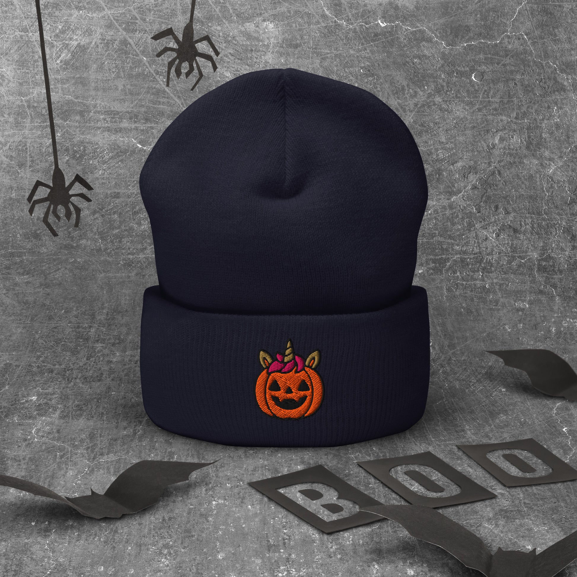 Black beanie with Halloween pumpkin design on a textured gray background with spider webs and 'BOO' letters.