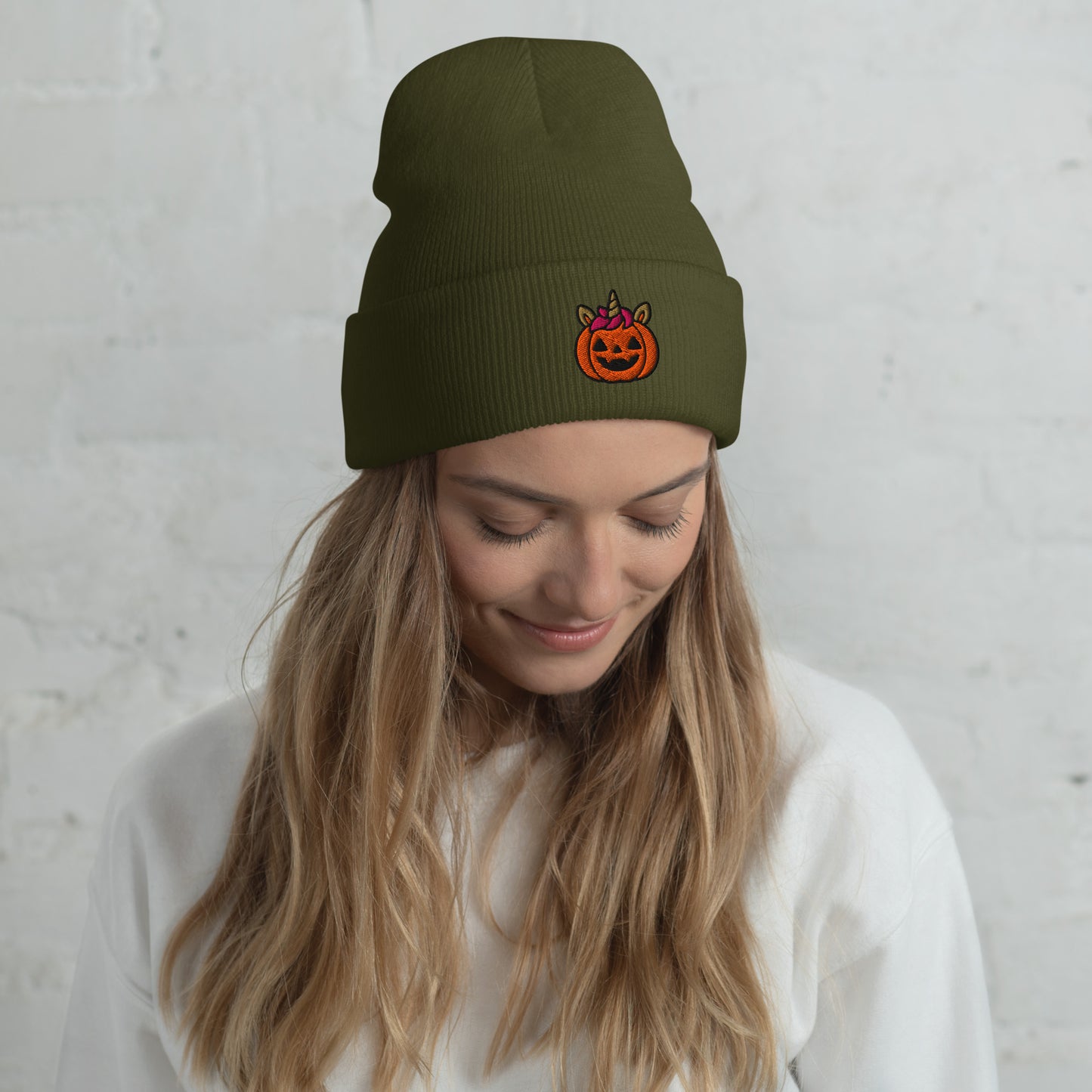 Woman wearing a green beanie with a pumpkin design against a light gray background