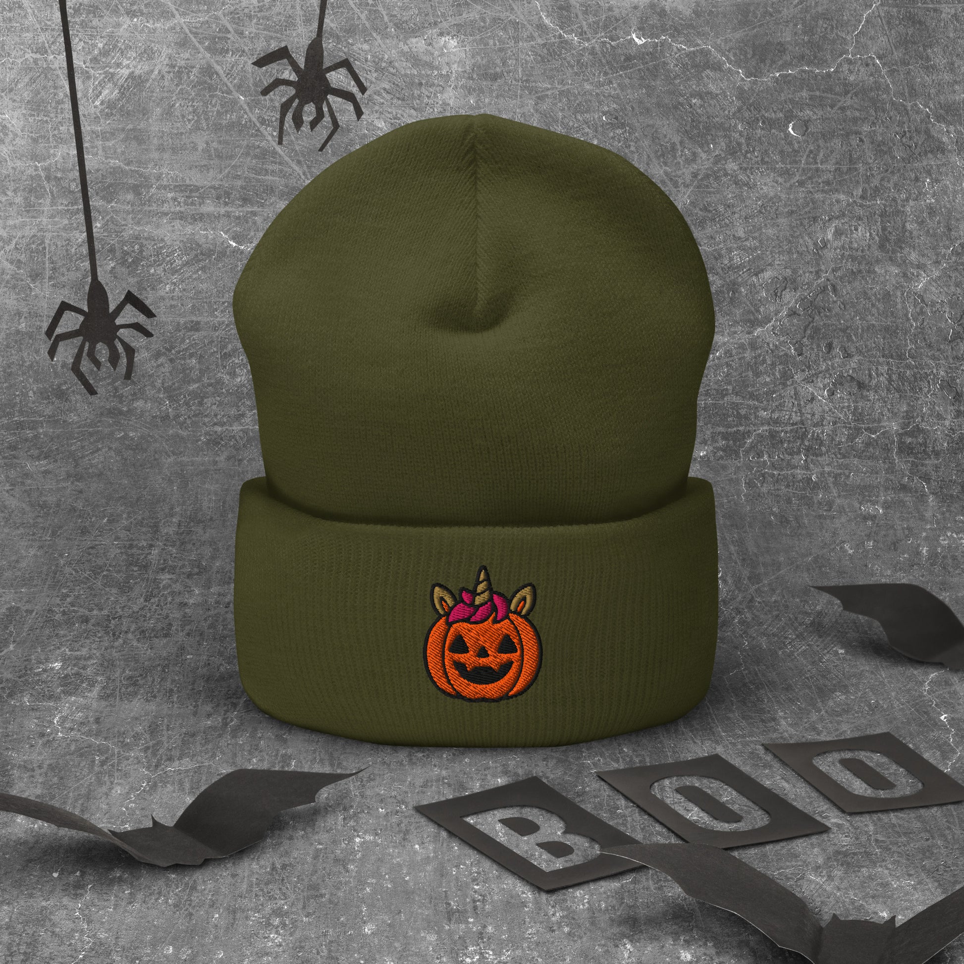 Green beanie with a Halloween pumpkin design on a textured gray background with spider webs and 'BOO' letters.
