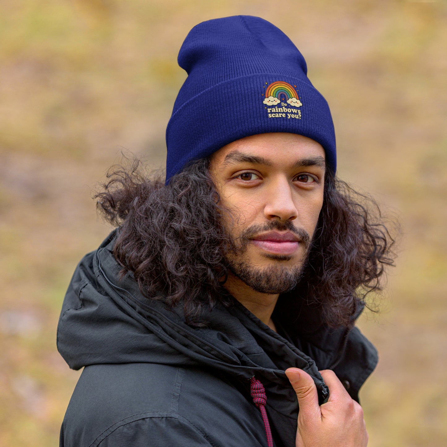 Person wearing a blue beanie with a rainbow design and text, outdoors.