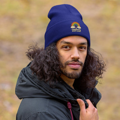 Person wearing a blue beanie with a rainbow design and text, outdoors.