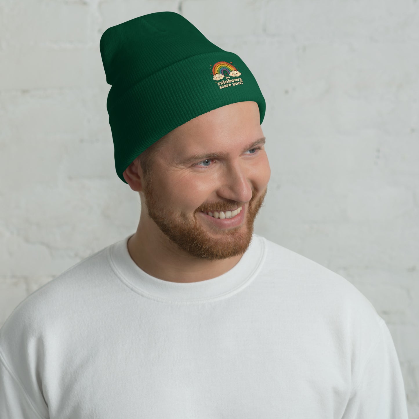 Man wearing a green beanie with a rainbow design against a gray wall