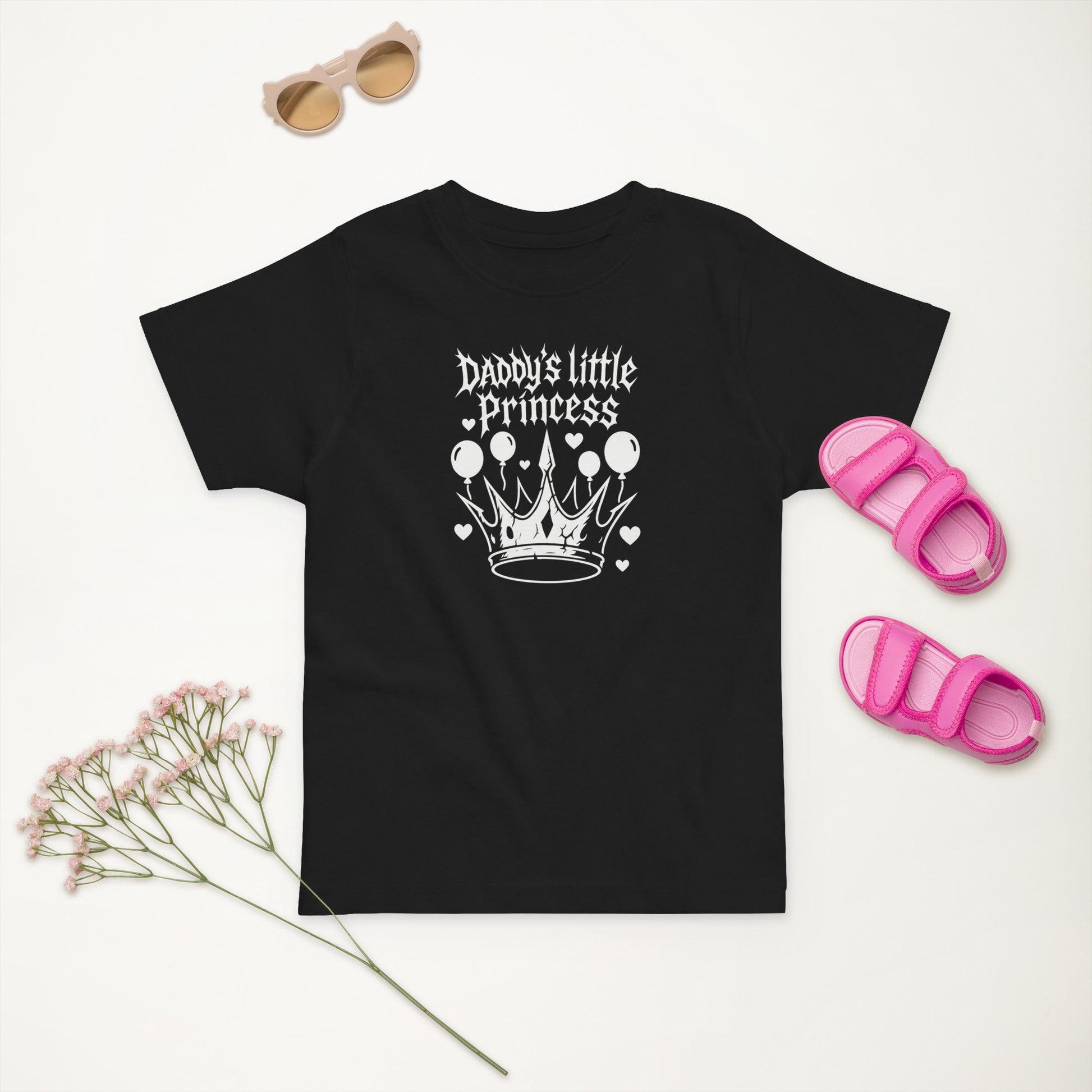 Black t-shirt with 'Daddy's little Princess' design, sunglasses, pink sandals, and dried flowers on a white background