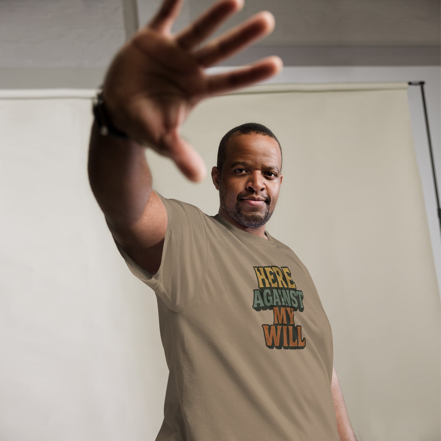Man wearing a beige t-shirt with text, extending his hand towards the camera.