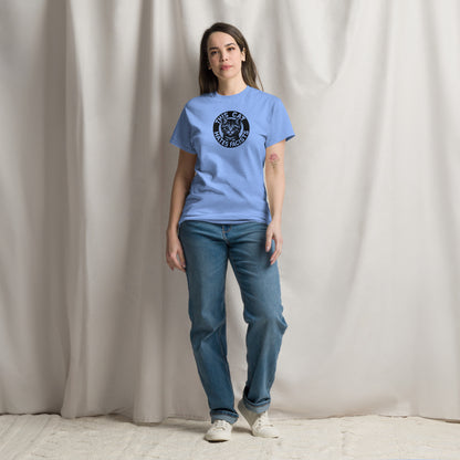 Person wearing a light blue t-shirt with a logo and blue jeans against a plain background