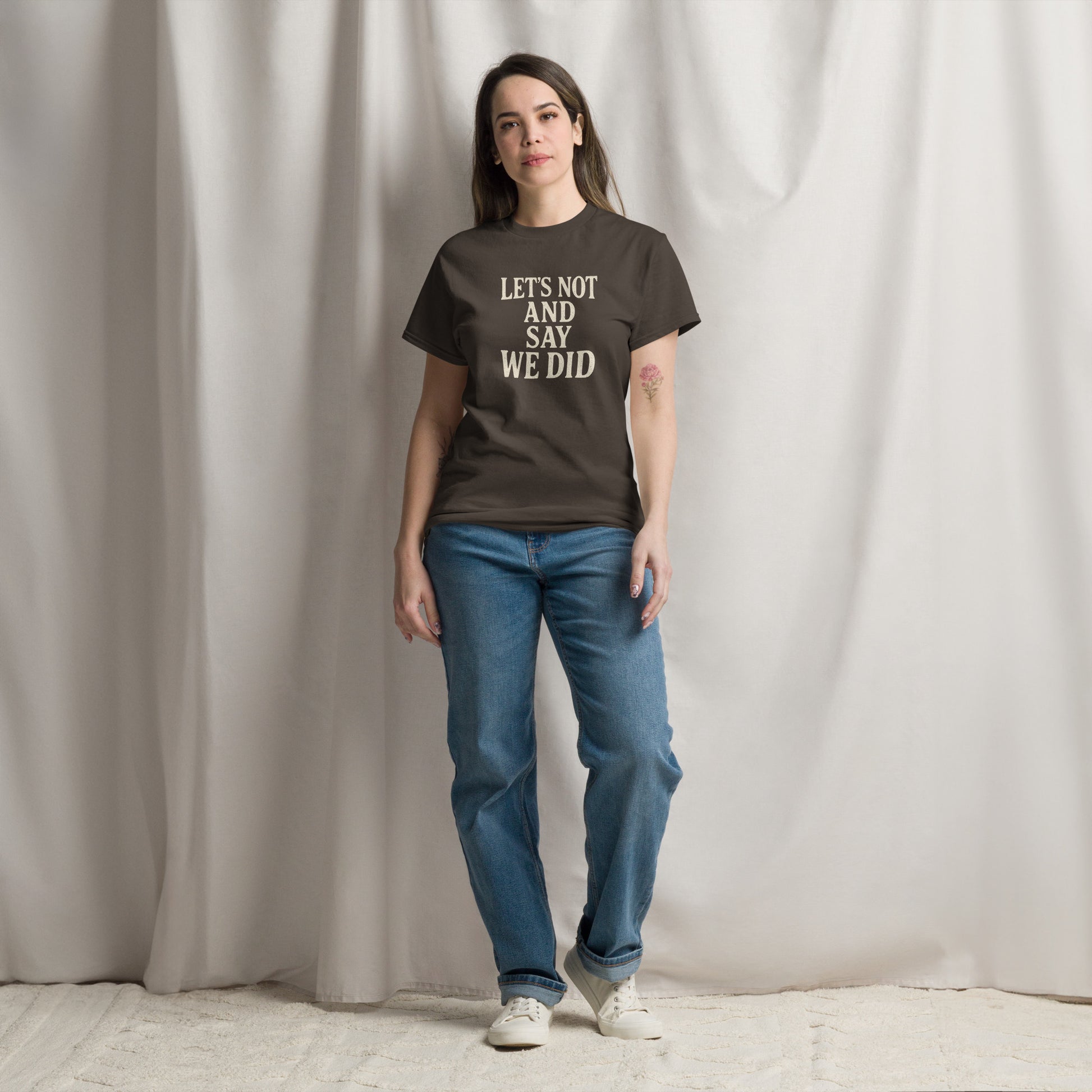 Person wearing a brown t-shirt with text and blue jeans standing against a plain background