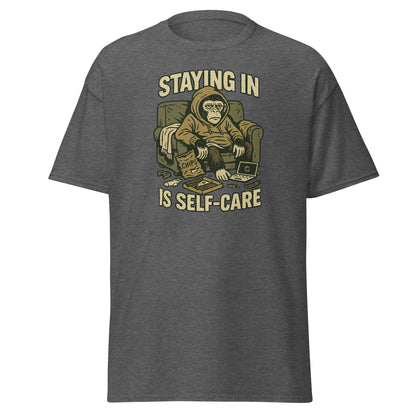 Gray t-shirt with a graphic of a monkey in a chair and text 'STAYING IN IS SELF-CARE' on a white background.