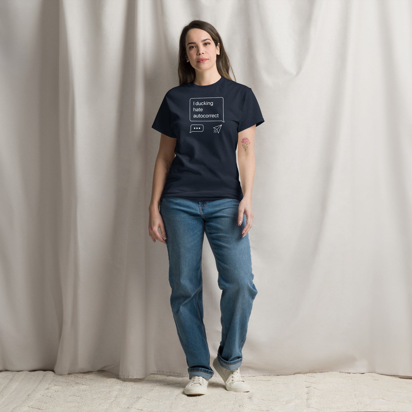 Person wearing a black t-shirt with text and blue jeans against a plain background