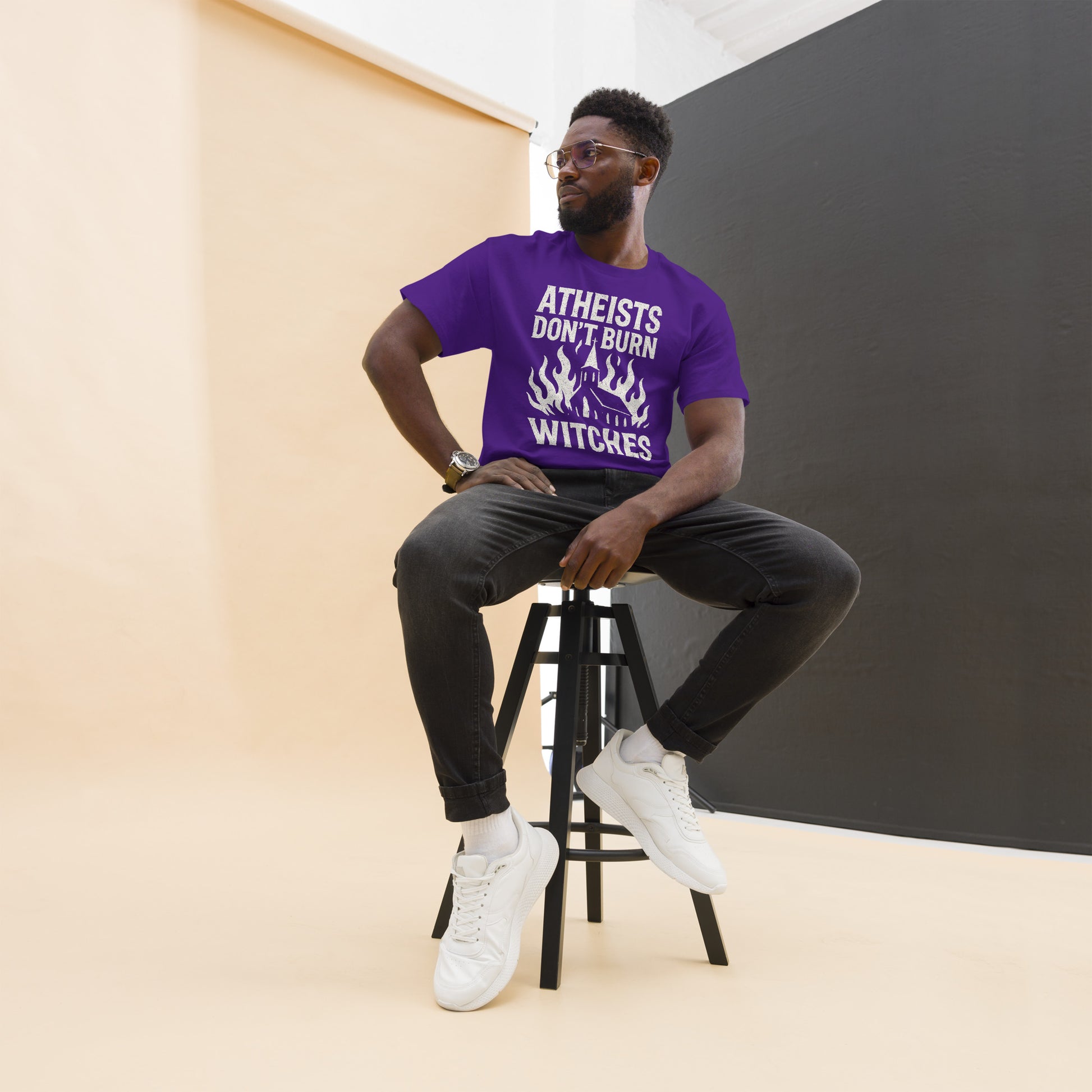 Person wearing a purple t-shirt with text sitting on a stool against a plain background