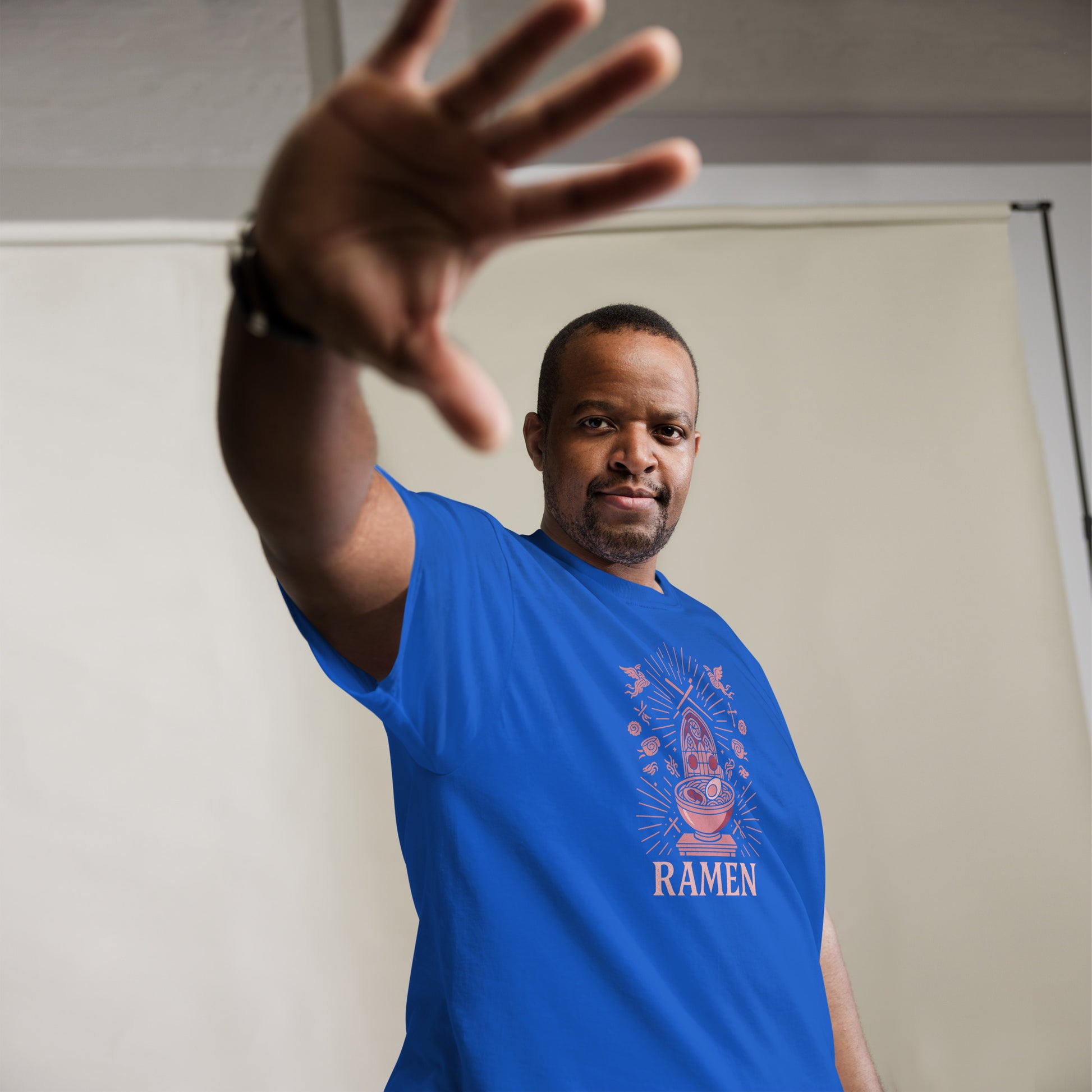 Man wearing a blue t-shirt with 'RAMEN' design, reaching out with his hand.
