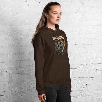 Woman wearing a brown hoodie with a graphic design against a white brick wall.