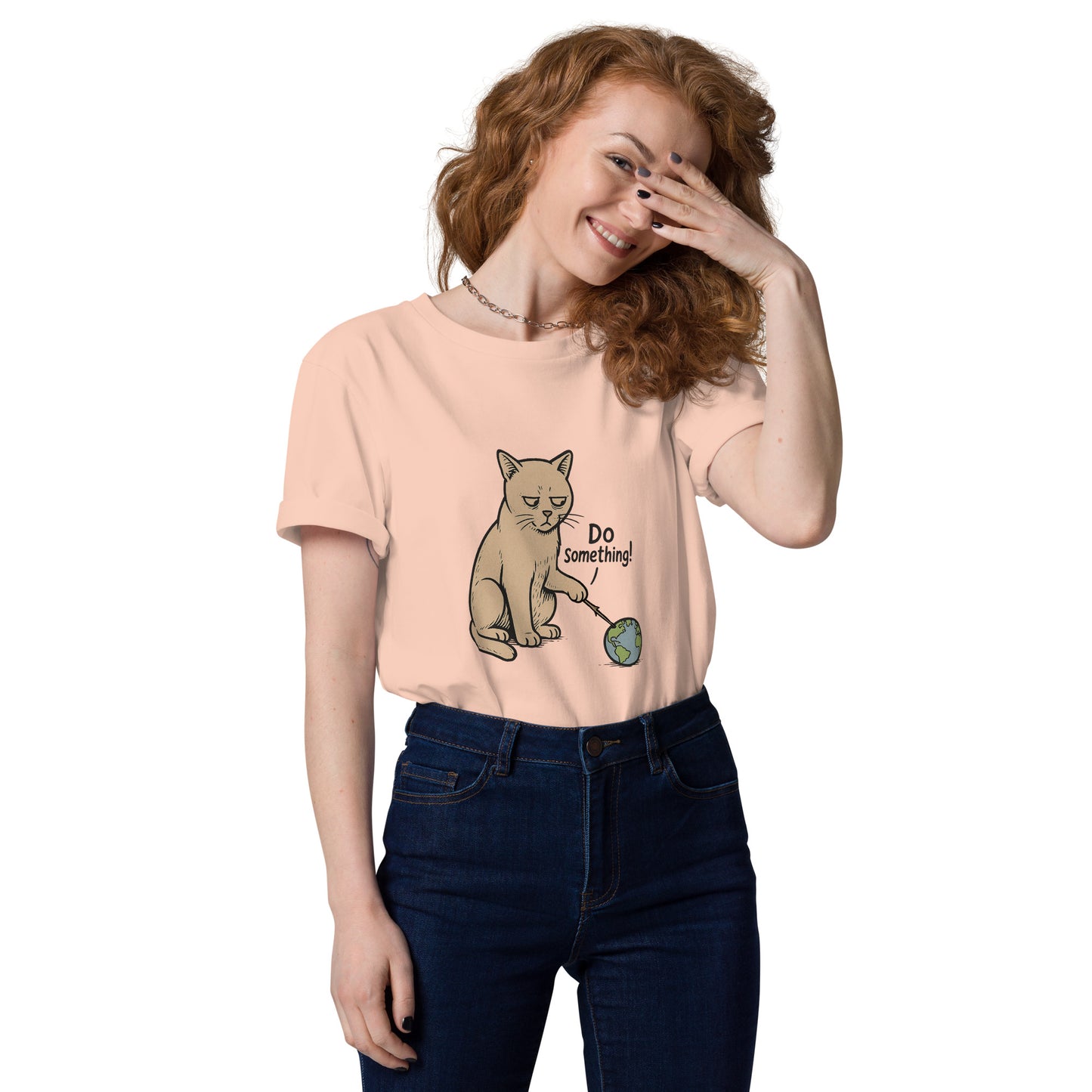 Woman wearing a peach t-shirt with a cat graphic and text, smiling and covering her face with one hand.