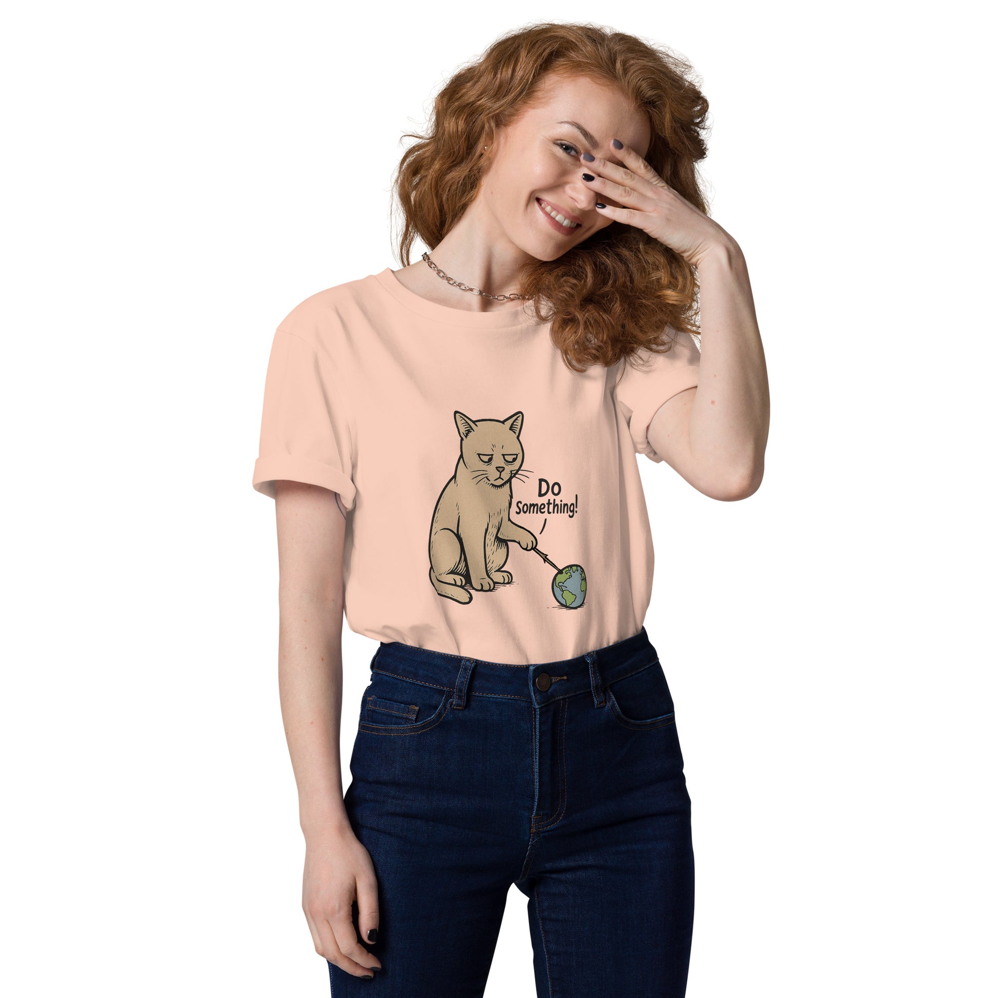 Woman wearing a peach t-shirt with a cat graphic and text, smiling and covering her face with one hand.