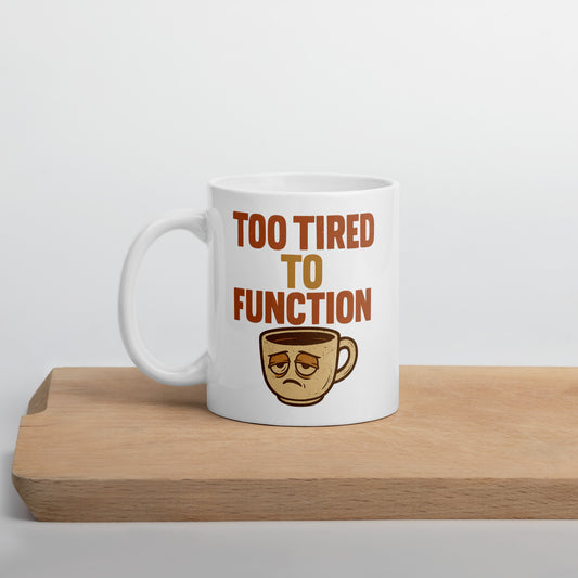 White mug with 'Too Tired to Function' text and coffee cup graphic on a wooden surface.