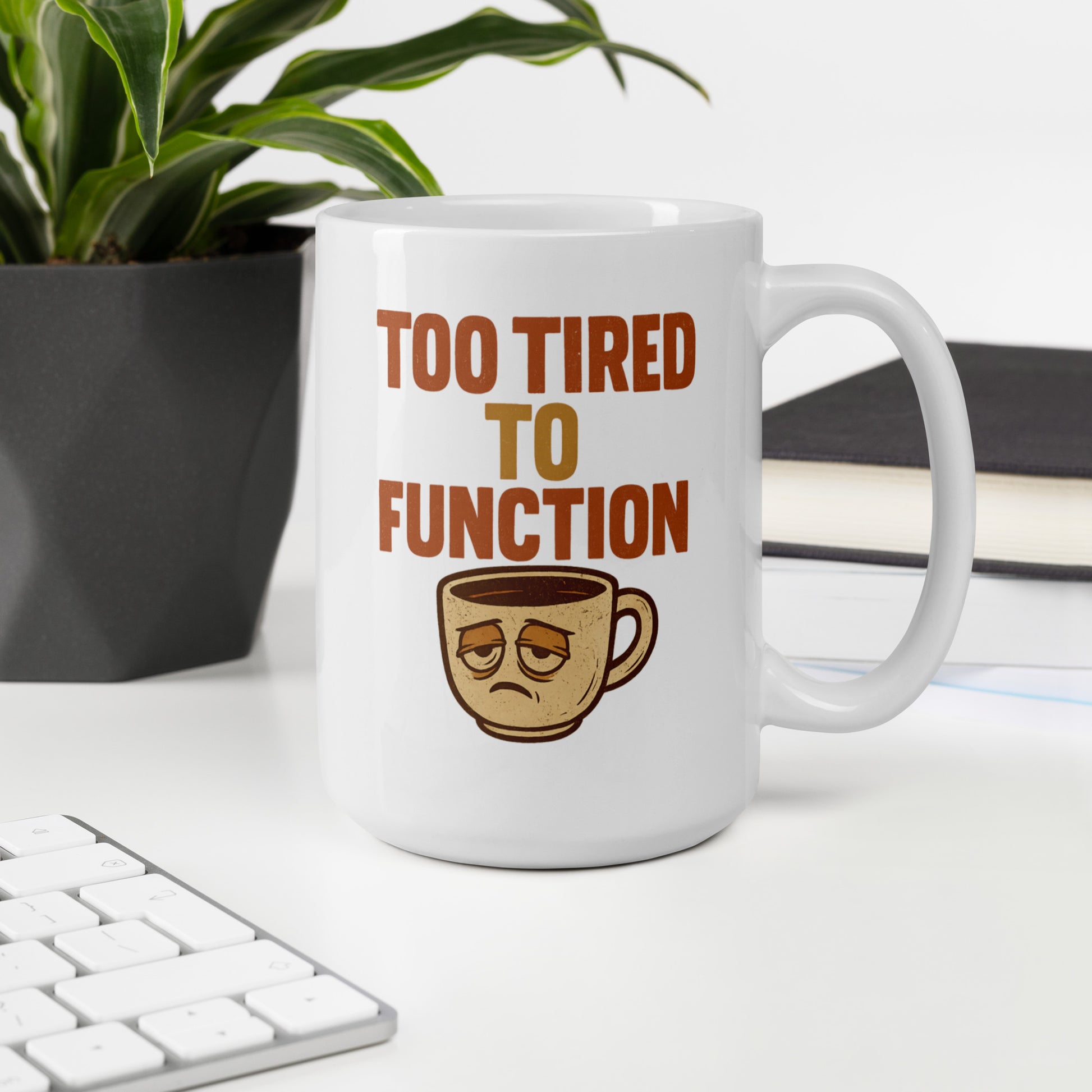 White mug with 'Too Tired to Function' text and coffee cup emoji on a desk with a plant and books in the background.